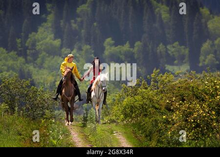 Le couple kazakh en costumes nationaux main dans la main sur leur cheval à Almaty, Kazakhstan. Banque D'Images