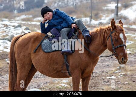 Jeune garçon nomade allongé sur le cheval et me regarde, près de Bichkek, au Kirghizistan Banque D'Images