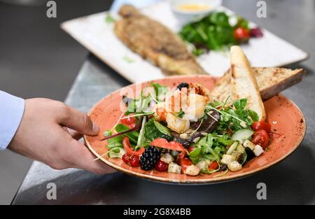 20 juillet 2021, Brandebourg, Potsdam : une salade de crevettes et de truite est servie au restaurant 'Kongsnaes - la gare impériale de Sailor'. Le restaurant Laggner Group, construit en bois norvégien, est situé sur la Jungfernsee. Il sert principalement du poisson, principalement régional, ainsi que des plats de bouillabaisse et de saison. En 1890, le Kaiser Wilhelm II fit reconstruire sa station de voile sur la Jungfernsee de Potsdam dans le style dragon 'norvégien'. Après un incendie dans les jours de guerre. En 1945, les fortifications frontalières de la RDA se sont encouru le long de ce site. Avec l'aide de plans historiques et de photographies, les contre Banque D'Images