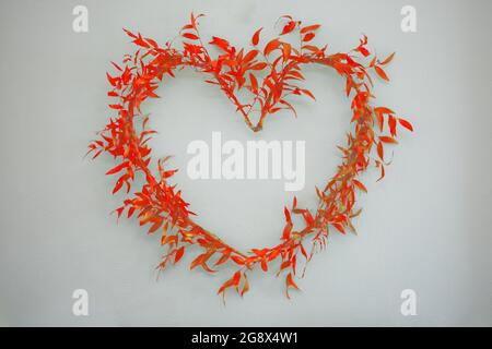 Symbole de coeur arrangé des branches de ruscus avec des feuilles rouges sur un fond clair. Banque D'Images