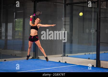 Femme jouant de padel dans un terrain de padel d'herbe bleue intérieur - jeune femme sportive joueur de padel frappant le ballon avec une raquette Banque D'Images