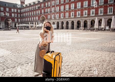 Voyage d'été pendant le Covid-19 et le tourisme. Triste femme touristique avec des bagages et un masque de visage ne pouvait pas aller à l'étranger pendant les vacances d'été. Coffre-fort après Covid Banque D'Images