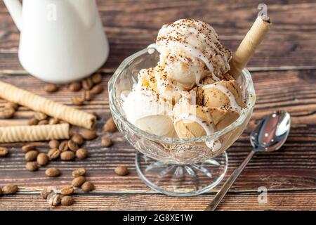 Glace Roma au noyer, à la crème et au caramel dans un bol en verre avec du café moulu et de la sauce au chocolat blanc. Banque D'Images