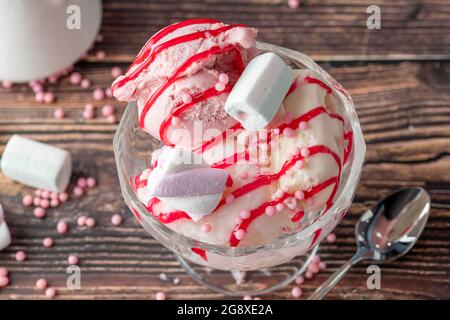 Crème glacée Roma à la fraise, à la banane et à la crème dans un bol en verre avec sauce rouge versée dessus. Banque D'Images