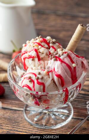 Crème glacée Roma à la fraise, à la banane et à la crème dans un bol en verre avec sauce rouge versée dessus. Banque D'Images
