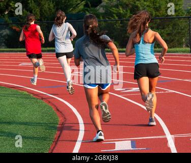 Vue arrière d'un groupe de filles de lycée qui s'exécutent rapidement sur une piste pendant les entraînements de camp d'été. Banque D'Images