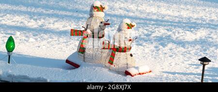 Deux bonhommes de neige sur un traîneau dans la décoration de neige sur une pelouse devant. Banque D'Images