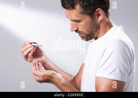 Homme dans un T-shirt blanc utilisant un compte-gouttes d'huile facial pour faire tomber le liquide dans ses mains. Banque D'Images