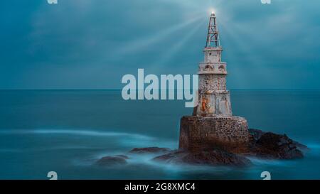 Ancienne tour de phare blanche isolée dans l'eau de mer bleu calme après le coucher du soleil près d'Ahtopol sur la côte de la mer Noire, Bulgarie. Paysage de phare émettant li Banque D'Images