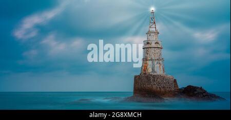 Vue à angle bas de l'ancienne tour de phare blanc isolée dans l'eau de mer bleu calme après le coucher du soleil près d'Ahtopol sur la côte de la mer Noire, Bulgarie. Paysage de lumière Banque D'Images