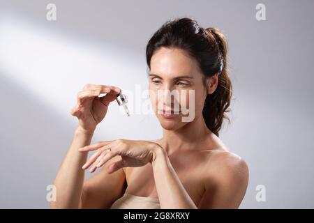 Une jeune femme utilisant un compte-gouttes liquide pour appliquer des soins de la peau à ses mains. Banque D'Images