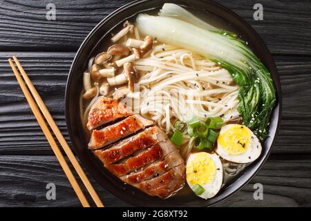 Ramen japonais maison avec canard, champignons, œufs et chou pak choi dans un bol sur table noire. Vue horizontale du dessus Banque D'Images