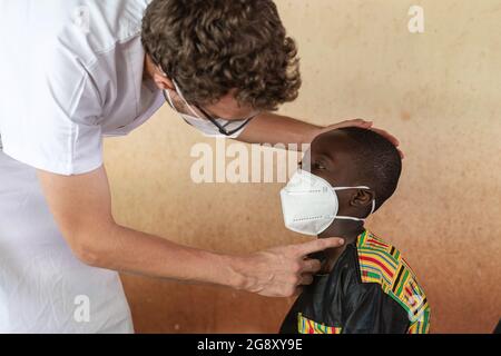 Dans cette image, un médecin caucasien dans un manteau de laboratoire blanc est de vérifier la gorge d'un garçon d'école noir de douleur avec des ganglions lymphatiques enflés comme une possible sy Banque D'Images