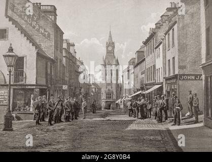 Vue de la fin du XIXe siècle sur High Street à Dunfermline, une ville et l'ancien Royal Burgh à Fife, en Écosse. Au bout de la rue bondée se trouve Dunfermline City Chambers, conçu par James Campbell Walker dans le style gothique français, et achevé en mai 1879. Il a été construit pour remplacer la vieille maison de ville après une croissance industrielle rapide dans la région. Banque D'Images