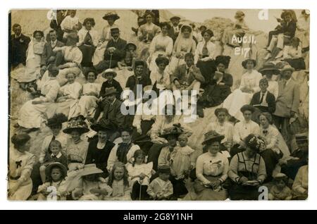 Carte postale Edwardienne de la fête des amateurs de plage assis sur des rochers lors d'une sortie du dimanche, portant leur meilleur dimanche, photo des photographes de plage Phillipse & Lees, Ilfracombe, Devon, Royaume-Uni datée d'août 11 1910 Banque D'Images