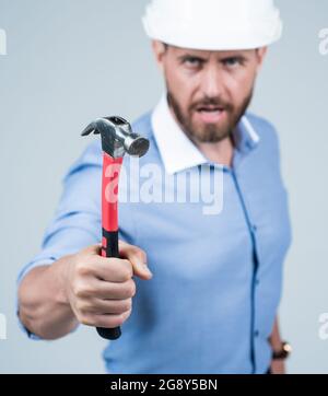 marteau en main de l'homme d'affaires mûr en colère dans le casque, foyer sélectif, colère et agression. Banque D'Images