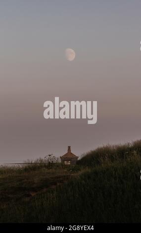 Belle lune s'élevant au-dessus d'une maison de bateau dans les dunes de sable de la côte britannique Banque D'Images