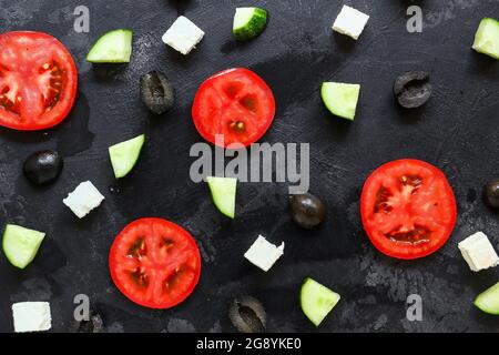 Ingrédients de salade César. Tomates en tranches, concombres, fromage feta et olives. Légumes frais sur fond sombre. Banque D'Images