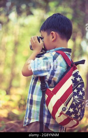 Garçon asiatique prenant des photos avec un appareil photo numérique professionnel en arrière-plan de jardin. Photo de style rétro. Enfant intelligent dans la nature. Portrait à l'extérieur. Photo dans Banque D'Images