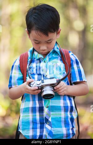 Smart boy asiatique vérifie et examine des photos dans un appareil photo numérique professionnel sur fond de nature. Un style de vie actif, la curiosité, la poursuite d'un hobby, te Banque D'Images