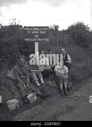 Dans les années 1950, historique, à l extérieur de la campagne, un petit groupe de personnes s assoient pour une photo par un panneau pour une voie publique de bride à Nore, Kent, Englod, Royaume-Uni. Nore est une longue rive de sable au rétrécissement de l'estuaire de la Tamise et un endroit un chemin de marche sur les North Downs. Banque D'Images