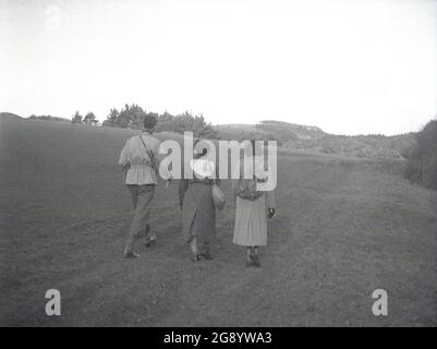 Années 1950, historique, un homme et deux dames, tous deux portant un long manteau et un avec un sac à dos en toile sur son dos, en marchant sur les bas sud à Beachy Head, près d'Eastbourne, East Sussex, Angleterre, Royaume-Uni. Un promontoire avec la plus haute falaise de la mer de craie en Grande-Bretagne, c'est un endroit célèbre pour la promenade de plaisir, avec une vue magnifique sur la Manche. Une zone d'une beauté naturelle exceptionnelle, en 1929, une loi du Parlement, a permis l'achat des terres pour protéger et sauvegarder leur utilisation pour les générations futures. Banque D'Images