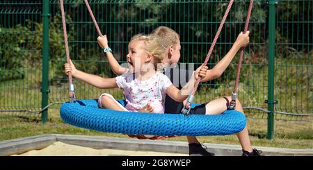 Enfants sur une balançoire. Un jour d'été, un garçon et une fille se balancent dans le parc. Balancer dans le parc d'attractions pour enfants. Bannière avec place pour le texte Banque D'Images