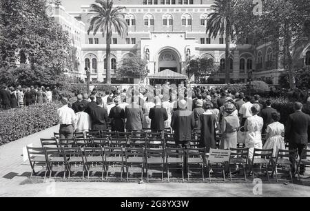 1964, historique, à l'Université de Californie du Sud (USC) une cérémonie de remise des diplômes a lieu, Californie, États-Unis, avec des parents et des invités debout à l'extérieur dans la zone réservée aux membres de la famille des diplômés d'honneur. Banque D'Images