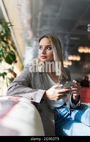 Femme d'affaires avec téléphone mobile contemplant tout en étant assise au café Banque D'Images