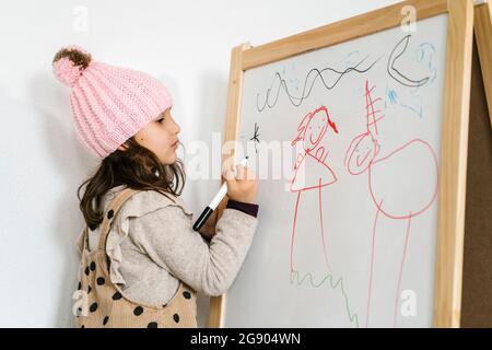 Fille avec chapeau en tricot à dessiner sur tableau blanc à la maison Banque D'Images