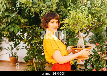 Femme souriante tenant Ficus Microcarpa plante par arbre dans l'arrière-cour Banque D'Images