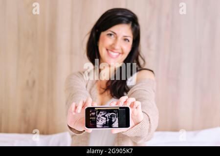 Femme enceinte souriante montrant une échographie sur un téléphone portable Banque D'Images