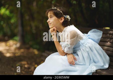 Fille en communion blanche robe de jour rêvant tout en étant assis sur le banc de parc Banque D'Images