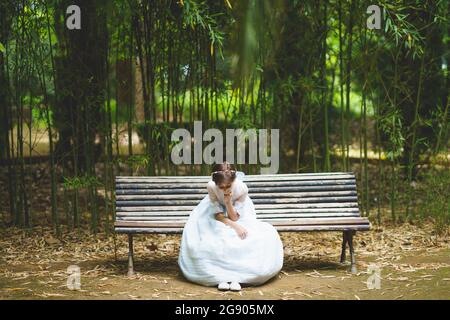 Fille à la main sur le menton en robe blanche de communion assise sur le banc dans le parc Banque D'Images