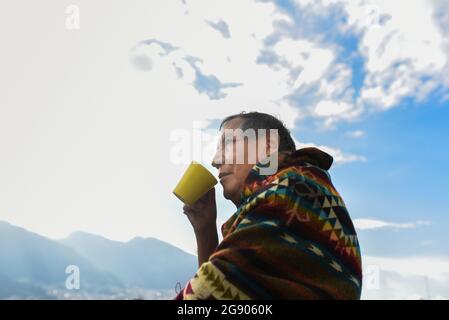 Homme portant un poncho traditionnel en regardant loin tout en buvant du café Banque D'Images