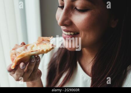 Femme souriante mangeant une tranche de pizza à la maison Banque D'Images