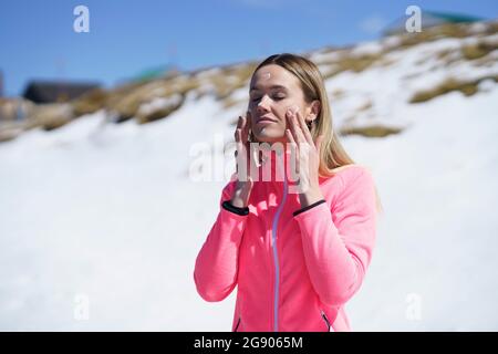 Jeune femme blonde appliquant de la crème solaire devant la montagne enneigée Banque D'Images