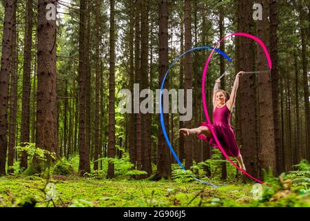 Gymnaste féminine souriante faisant de la gymnastique rythmique avec des rubans en forêt Banque D'Images