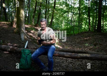 Un randonneur à l'aide d'une tablette numérique assis sur un arbre tombé Banque D'Images