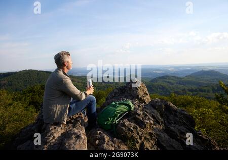 Randonneur mâle mature assis avec une bouteille d'eau et un sac à dos au sommet de la montagne Banque D'Images