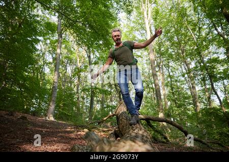 Homme aux bras étirés marchant sur un arbre tombé dans la forêt Banque D'Images