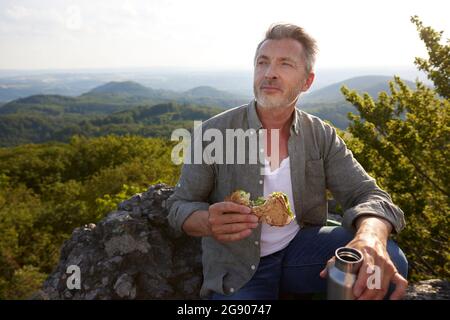 Randonneur mâle tenant un sandwich et une bouteille d'eau à la montagne Banque D'Images