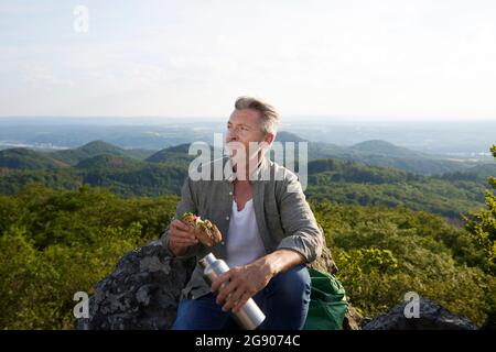 Randonneur mâle avec nourriture et bouteille assis au sommet de la montagne Banque D'Images