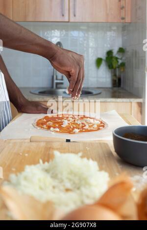 Homme en cuisine à la maison pour la garniture de pizza avec des oignons hachés Banque D'Images