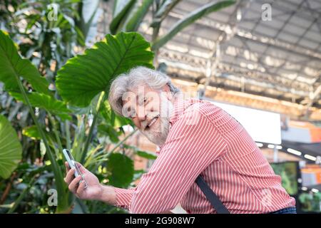 Heureux homme mature tenant un smartphone tout en se penchant à la gare Banque D'Images