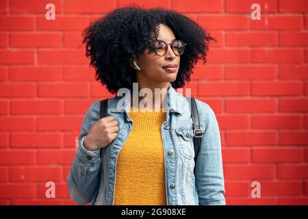 Une jeune femme attentionnés qui regarde loin devant le mur rouge Banque D'Images