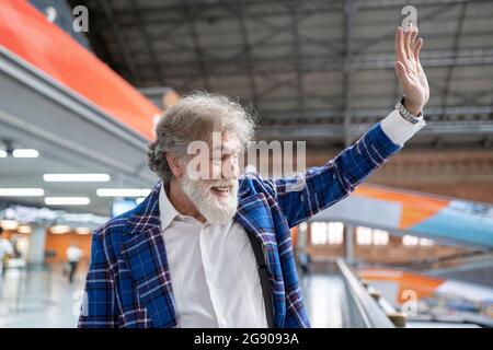 Homme mature à barbe blanche agitant la main en se tenant à la gare Banque D'Images