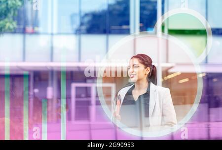 Femme d'affaires avec icônes de maison intelligente devant le bâtiment de bureau Banque D'Images