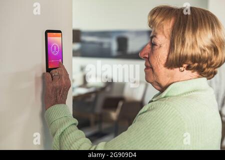 Femme âgée utilisant un thermostat intelligent au mur à la maison Banque D'Images