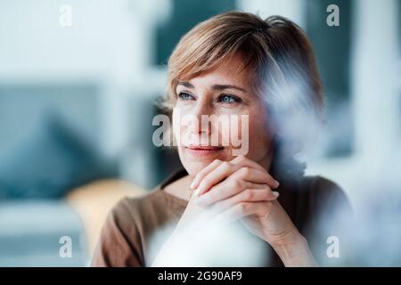 Femme d'affaires réfléchie avec les mains jointes dans le bureau Banque D'Images